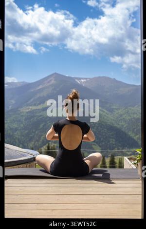 Femme méditant face aux montagnes des Carpates. Vue arrière d'une femme assise les jambes croisées sur un tapis de yoga sur une terrasse en bois, face à l'ukrainien vert Banque D'Images