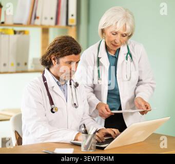 Femme âgée et médecins adultes travaillant sur ordinateur portable dans le cabinet médical Banque D'Images