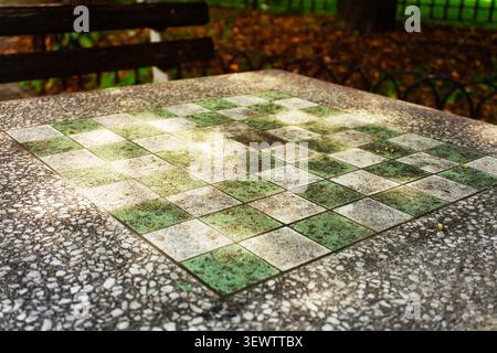 Un échiquier extérieur altéré sur une table en pierre dans un cadre de parc en automne. Banque D'Images