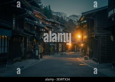 Vue sur la station historique Narai-juku à Shiojiri, avec des bâtiments traditionnels en bois illuminés par les lumières chaudes du soir le long d'une rue calme Banque D'Images