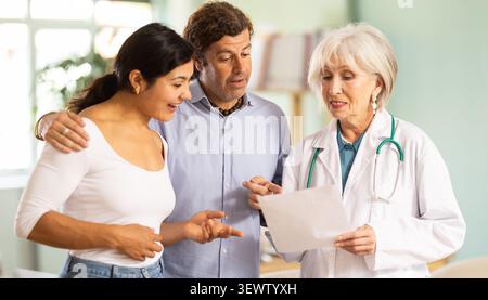 Médecin âgé discutant des tests médicaux avec un couple heureux au cabinet médical Banque D'Images
