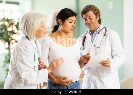 Femme enceinte heureuse discutant des résultats des tests médicaux avec deux médecins Banque D'Images