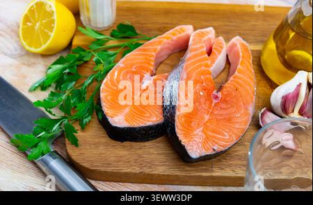 Steaks de saumon crus sur une planche à découper en bois avec des légumes verts, du citron et de l'ail Banque D'Images