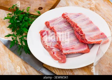Côtes de porc fraîches sur plaque en céramique blanche avec persil sur table Banque D'Images