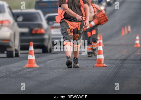 Travailleurs routiers plaçant des cônes de circulation pendant la réparation d'une route asphaltée dans une rue fréquentée de la ville. Concept de fermeture de voie, entretien des routes, contrôle du trafic, const Banque D'Images