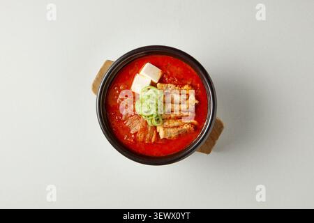 Ragoût de tofu épicé coréen sundubu jjigae servi dans un pot traditionnel en faïence noire avec tofu, kimchi et oignon vert sur fond gris Banque D'Images