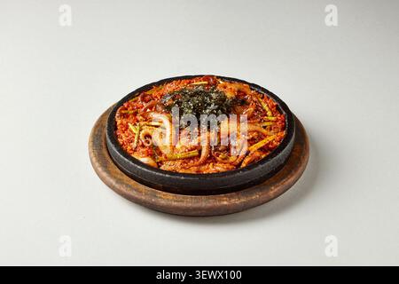 Nouilles sautées coréennes épicées avec fruits de mer servies dans une casserole traditionnelle en pierre noire sur fond gris clair, photographie culinaire coréenne Banque D'Images