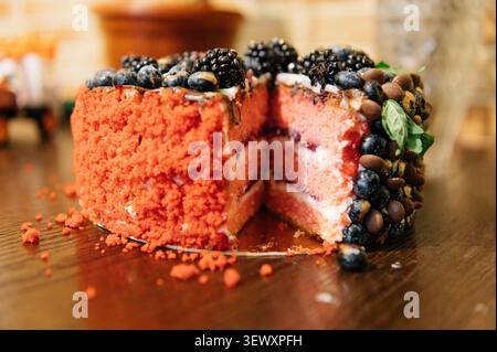 Gros plan d'un gâteau éponge rouge vif partiellement tranché décoré de myrtilles fraîches, de mûres et de morceaux de chocolat, servi sur un bois Banque D'Images