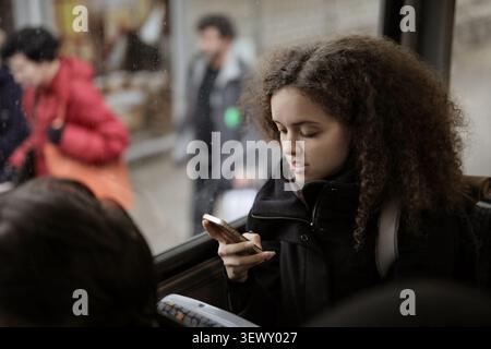 Une femme aux cheveux bouclés regarde son téléphone dans le bus Banque D'Images