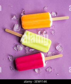 Trois popsicles colorés avec de la glace sur un fond violet Banque D'Images