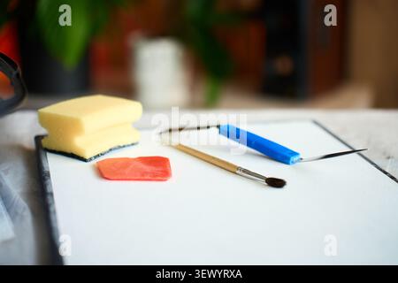 Les outils d'art sont disposés sur une toile vierge, avec couteau à palette, brosse, éponge et grattoir sur une feuille de protection. Concept de DIY texturé art et créatif Banque D'Images