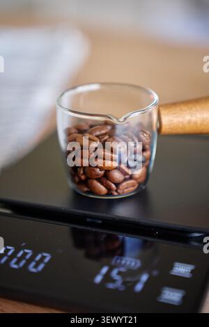 Grains de café sur échelle numérique dans une tasse en verre, mesurés avant la préparation manuelle. Concept de préparation du café et verser sur le café. Banque D'Images