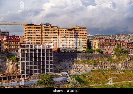 Chantier de construction urbaine avec de hauts bâtiments en développement. Les grues soulèvent des matériaux près d'une structure en béton non finie. Colline avec végétatio vert Banque D'Images