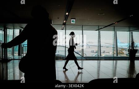 Silhouettes spectaculaires de personnes marchant à l'intérieur d'un terminal d'aéroport lumineux avec des avions visibles sur le tarmac à travers de grandes fenêtres en verre. Banque D'Images