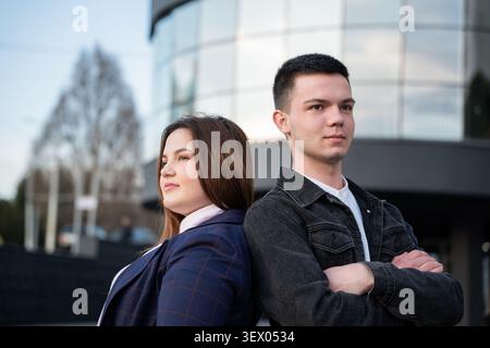 Jeunes collègues d'affaires debout dos à dos devant un immeuble de bureaux moderne dans un quartier d'affaires urbain. Coopération commerciale et professionnelle Banque D'Images