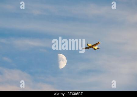 Avion léger volant près de la lune dans un ciel nuageux. Banque D'Images