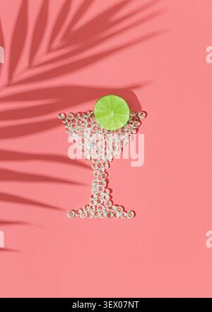 Composition d'été avec forme de verre martini faite de cristaux décoratifs avec tranche de citron vert frais sur fond rose pastel. Cocktail créatif et summe Banque D'Images