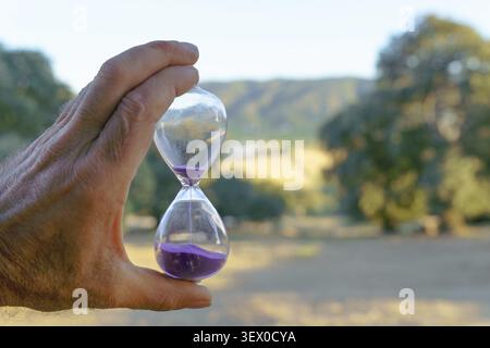 Ronda, malaga, espagne main humaine tenant un sablier avec du sable violet, symbolisant le concept du temps qui passe et des cycles de vie dans la nature Banque D'Images