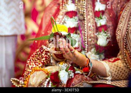 Mariée indienne en tenue traditionnelle effectue un rituel de mariage avec des fleurs et des feuilles Banque D'Images