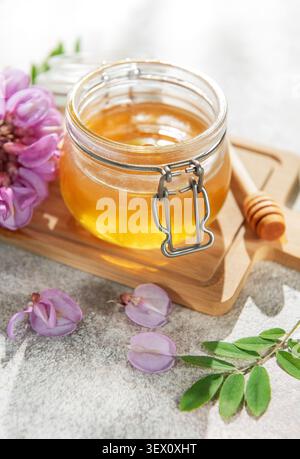Miel dans un bocal en verre avec des fleurs d'acacia rose et une benne en bois sur une planche Banque D'Images