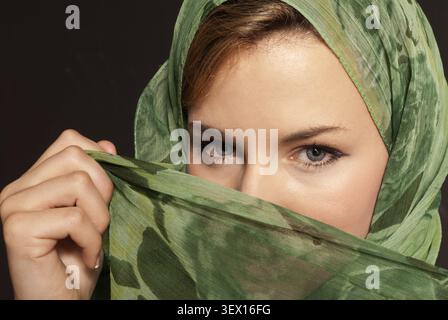 Jeune femme arabe avec voile montrant ses yeux sur fond gris foncé Banque D'Images