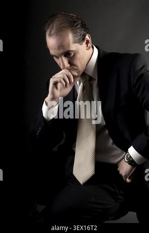 Homme d'affaires adulte pensée sérieuse assis sur fond sombre Banque D'Images