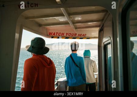Trois personnes se tiennent sur un bateau regardant au-dessus de l'océan sous un panneau Watch Your Head, sur le ferry pour le parc national des îles Anglo-Normandes, en Californie Banque D'Images