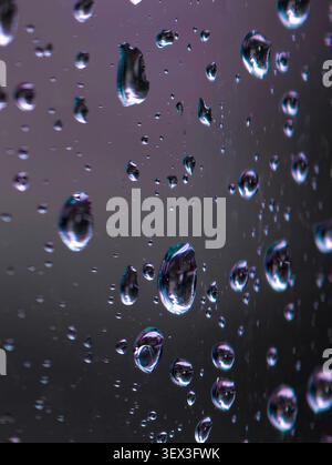 Des gouttelettes d'eau transparentes s'accrochent à la surface du verre, formant des reflets lumineux et des reflets doux sur le fond gris foncé, créant une texture abstraite de mauvaise humeur Banque D'Images