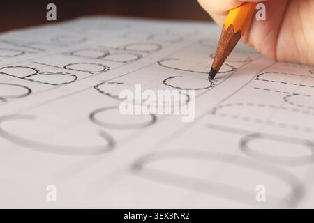 Gros plan d'un enfant apprenant à écrire dans une feuille de travail d'écriture manuscrite. Concept : apprendre, apprendre à écrire, alphabet, aide, écriture alphabet d'aide Banque D'Images