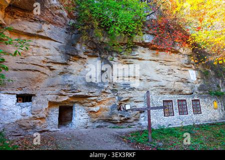 Monastère de la grotte de Saharna en Moldavie un ancien ermitage chrétien sculpté directement dans une falaise de calcaire massive. Grande croix en bois se tient près de la pierre Banque D'Images