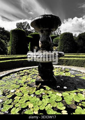 Fontaine de jardin ornementale traditionnelle en pierre à deux niveaux avec piédestal de balustre, feuillage sculpté, dans un jardin de parterre formel, couleur verte Banque D'Images