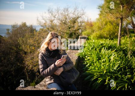 Femme utilisant la technologie à l'extérieur, s'engageant avec son appareil mobile dans un parc Banque D'Images
