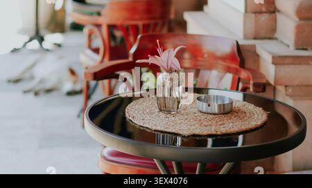 Lys rose dans un vase en verre sur une table de terrasse de café avec des meubles en bois Banque D'Images