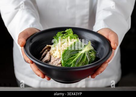 Chef tenant un bol ramen de bœuf avec nouilles et bok choy Banque D'Images