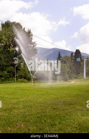 Bansko, Bulgarie cabines de télécabines bleues se déplaçant sur un champ verdoyant luxuriant avec un arroseur d'eau de travail contre les montagnes Pirin Banque D'Images