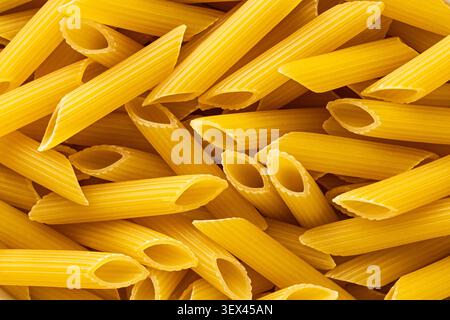 Macro texture proche des tubes de pâtes penne non cuites remplissant le cadre comme fond de nourriture sèche dorée Banque D'Images