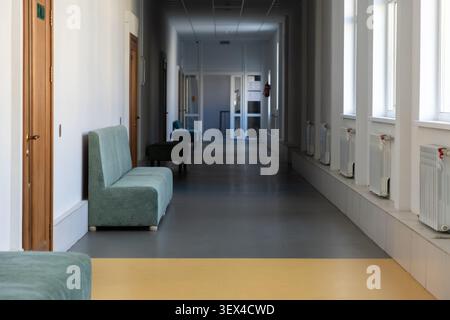 Long couloir dans un immeuble de bureaux contemporain avec des sièges doux pour les visiteurs, où la lumière vive et les tons discrets transmettent un sentiment de calme Banque D'Images