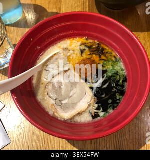Un appétissant bol de bouillon de porc crémeux ramen servi dans un bol rouge, évoquant des sentiments de satisfaction culinaire et de confort. Banque D'Images