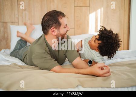 Père et fils allongés sur le lit, passant du temps de qualité ensemble et riant Banque D'Images