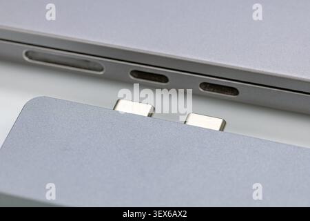 Macro détaillée gros plan montrant un adaptateur de concentrateur USB C double port en aluminium argenté aligné avec les ports Thunderbolt sur un ordinateur portable moderne, me mettant en évidence Banque D'Images