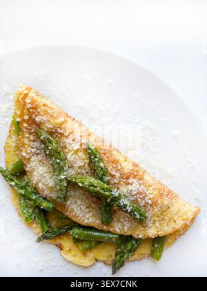 Omelette aux œufs pliée fourrée d'asperges vertes sautées et de parmesan râpé. Nourriture gastronomique saine sur fond blanc. Espace de copie, vue de dessus. Banque D'Images
