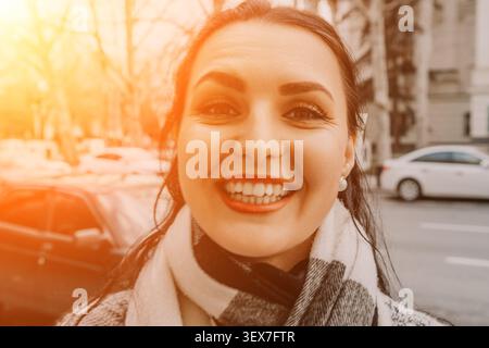 Femme souriante portrait en gros plan de femme heureuse avec rouge à lèvres rouge et foulard à carreaux sur la rue urbaine pendant l'heure d'or Banque D'Images