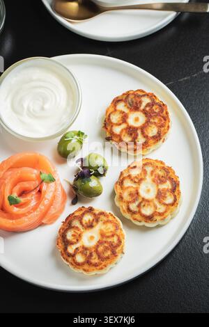 Salé Syrniki avec saumon fumé, olives et crème sure sur une assiette blanche Banque D'Images