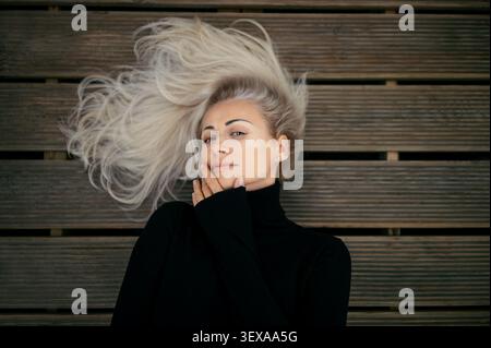 Belle femme blonde allongée sur un plancher en bois avec ses cheveux étendus, portant un col roulé noir Banque D'Images