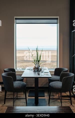 Élégante table à manger dans le restaurant scandinave, à côté d'une grande fenêtre donnant sur un champ désertique serein et décor minimaliste Banque D'Images