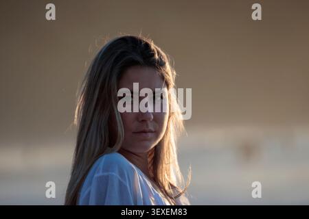 Femme posant pendant l'heure dorée, longs cheveux blonds illuminés par le contre-jour Banque D'Images