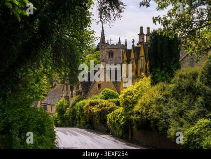 Charmante vue sur la flèche de l'église St Andrew s'élevant au-dessus des cottages en pierre classiques des Cotswold et de la végétation luxuriante à Castle Combe, en Angleterre. Banque D'Images