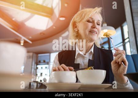 Femme senior savourant salade. Délices professionnels seniors dans une pause salade nutritive. Femme d'affaires mature dans Sunny Cafe interrompt le travail pour profiter Banque D'Images