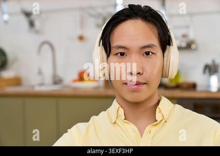 Un jeune homme asiatique se détend à l'intérieur portant des écouteurs dans une cuisine contemporaine Banque D'Images