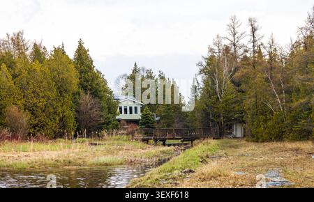 Une scène paisible au bord du lac mettant en scène une maison pittoresque nichée parmi des arbres luxuriants, capturant la tranquillité du printemps dans un cadre rural. Idéal pour les thèmes de Banque D'Images